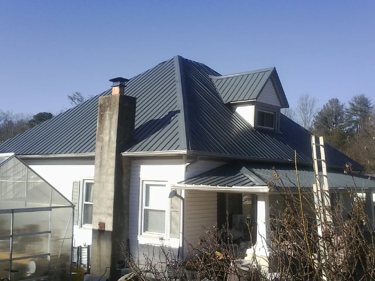 Dark blue standing seam metal roof on a white farmhouse with dormer — Slate & Tile Roof Repair by Roofing Brothers in Bussey