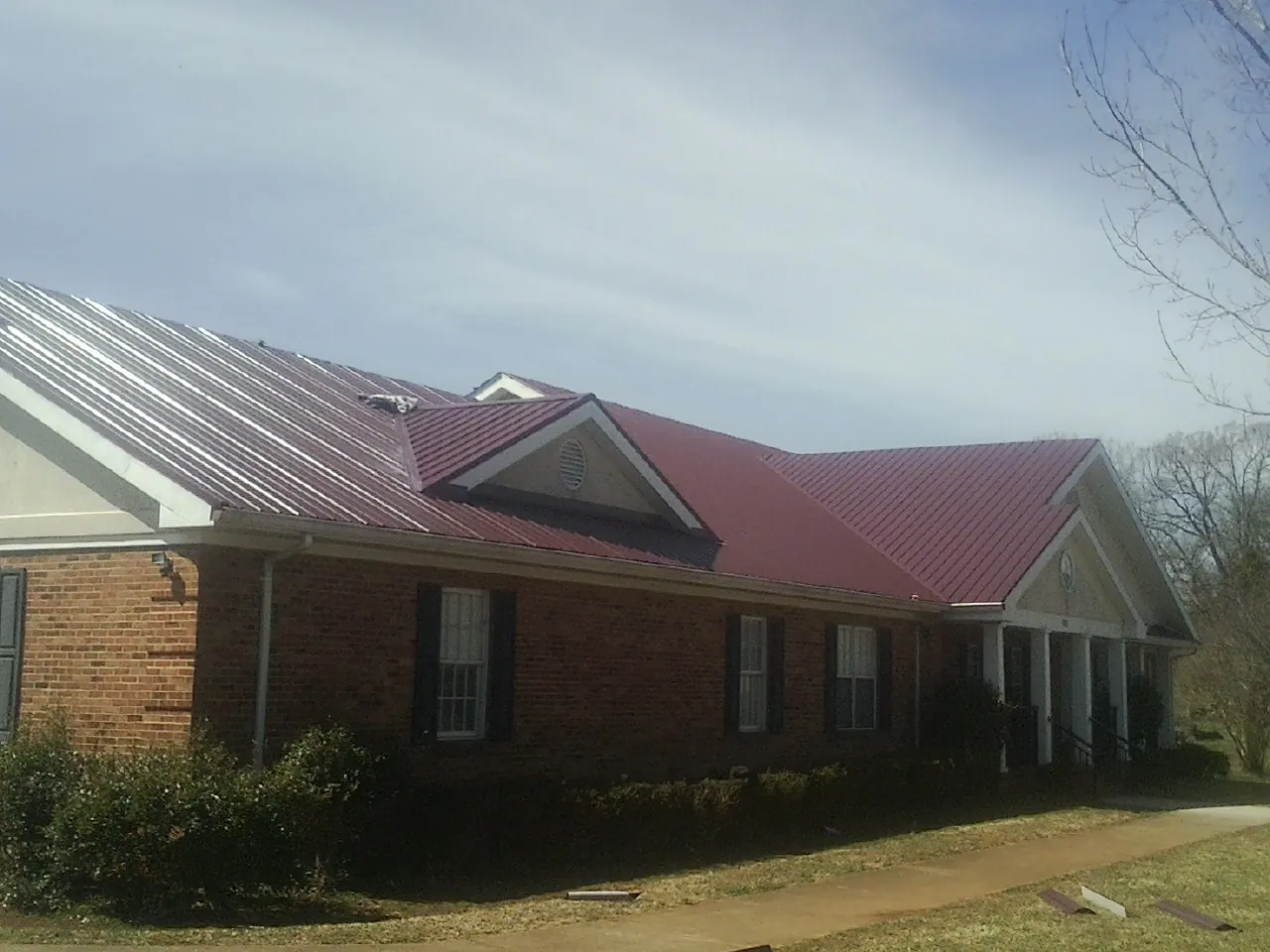 Red metal roof with gabled entries on a long brick building, from a Hail Damage Roof Repair job in Bussey