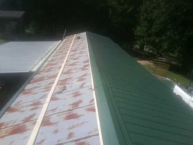 Old rusted panels beside newly installed green metal roofing — Wind Damage Roof Repair by Roofing Brothers in Bussey