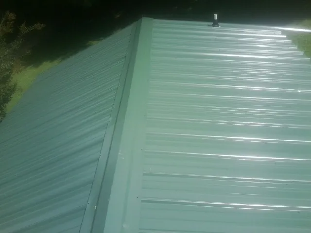 New green metal panels meeting at the ridge of a roof — Flat Roof Repair work by our crew in Bussey