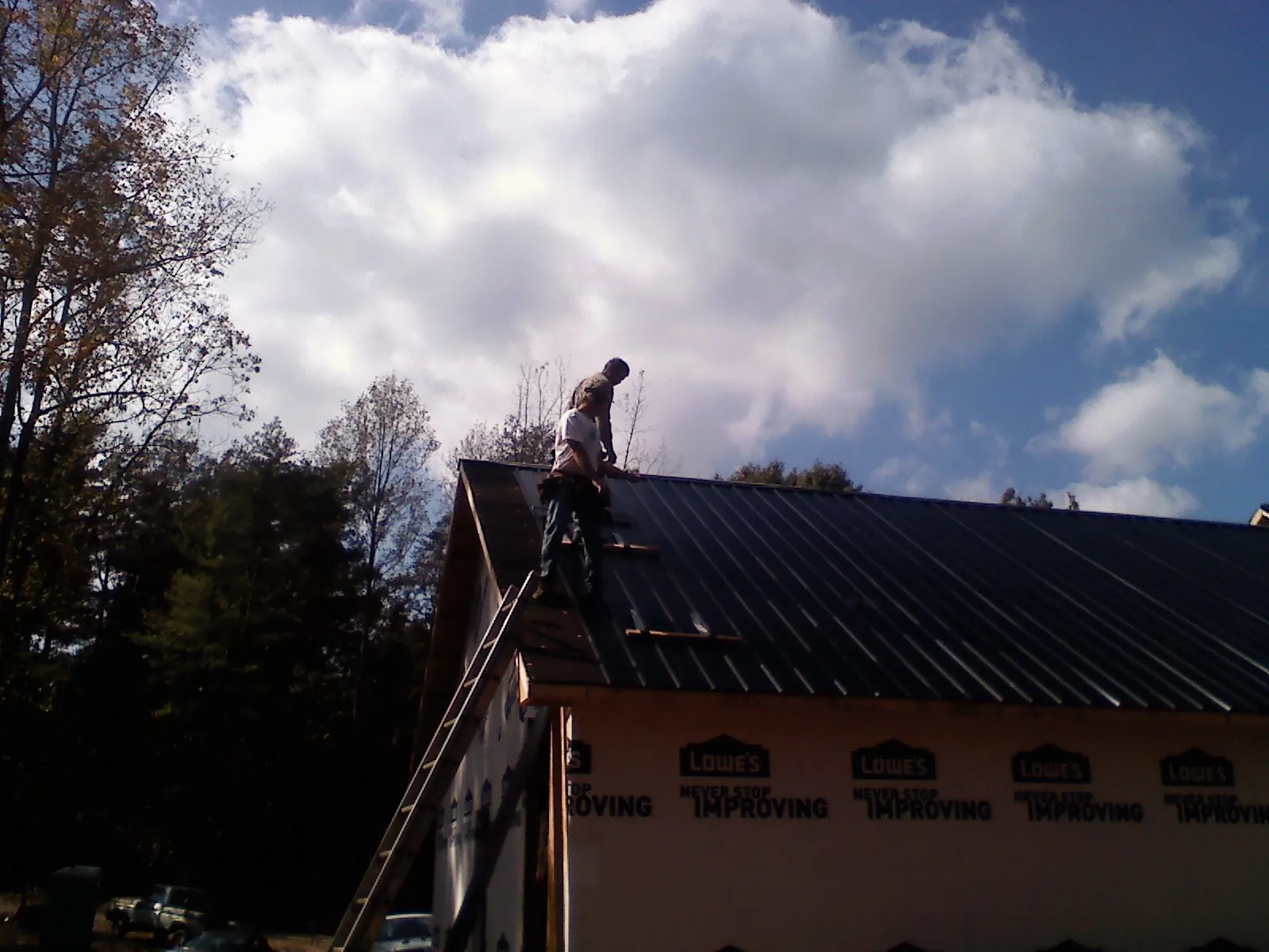 Roofer fastening dark metal panels high against a cloudy sky, from a Roof Inspection job in Bussey