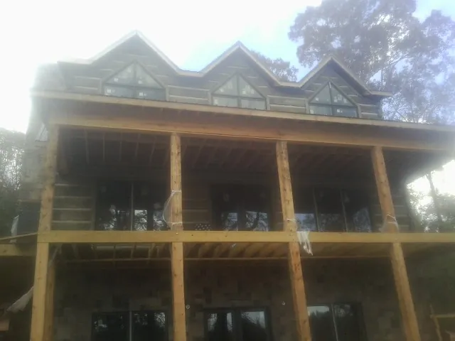 Dormers and porch framing on a large log home under construction — Roof Coating work by our crew in Bussey
