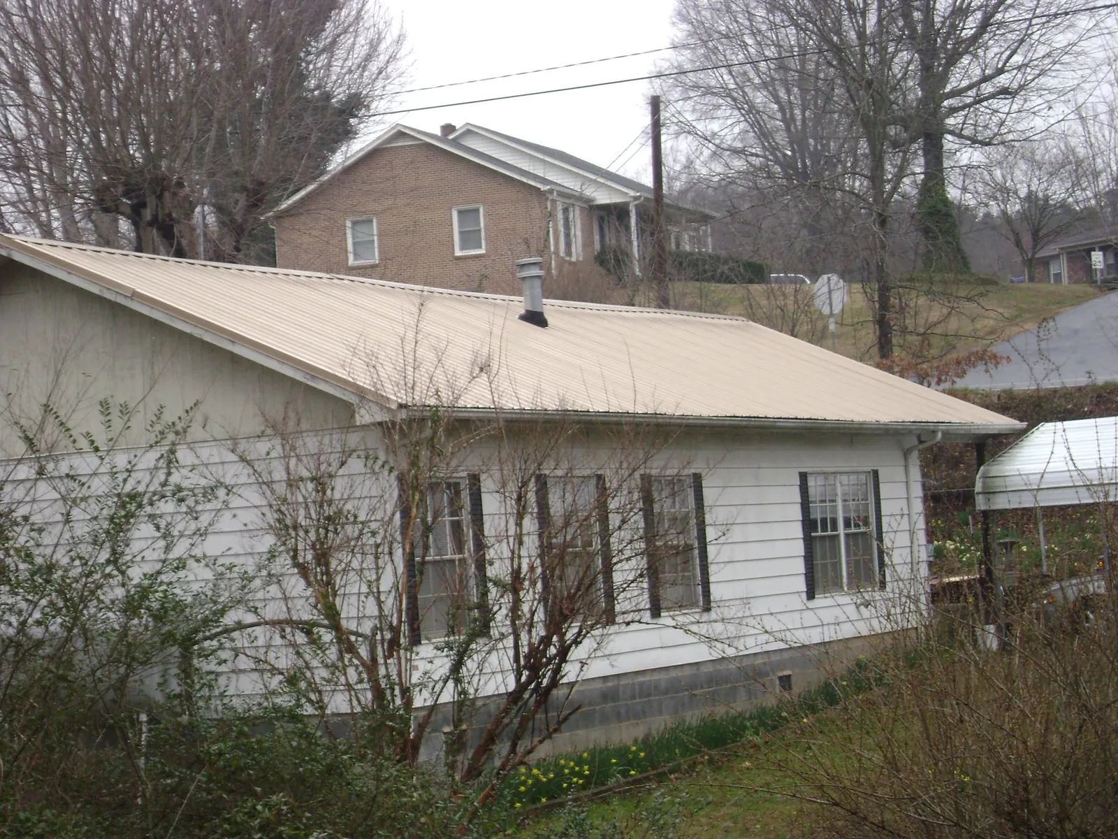 Tan metal roof on a white sided house set into a hillside — Commercial Roofing by Roofing Brothers in Bussey