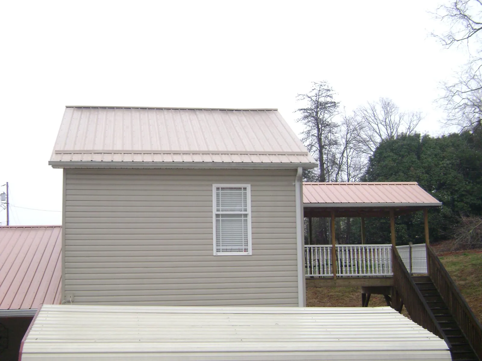 Tan metal roofs on a two story addition and attached porch, from a Roof Replacement job in Bussey